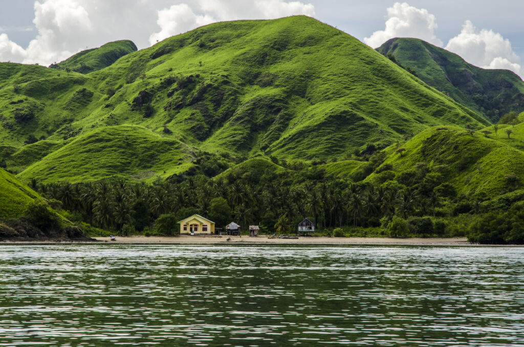 A yellow house across a body of water in front of a bright green mountain.