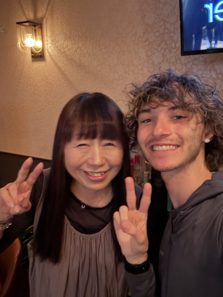 A student smiling with the owner of a karaoke establishment in Japan.
