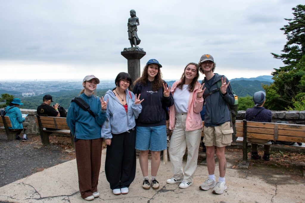 Five students are smiling for a photo with Mt.Takao in the background.