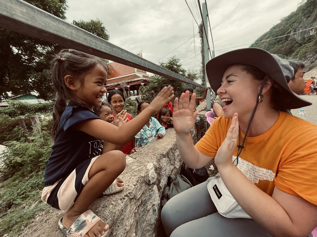 A girl in an orange shirt and gray bucket hat is high-fiving another girl. Both are smiling.