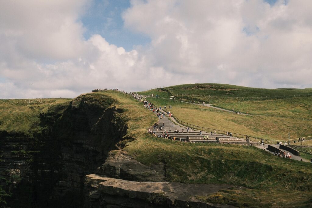 The Cliffs of Moher on a sunny day with clouds in the sky. Many people are visiting.