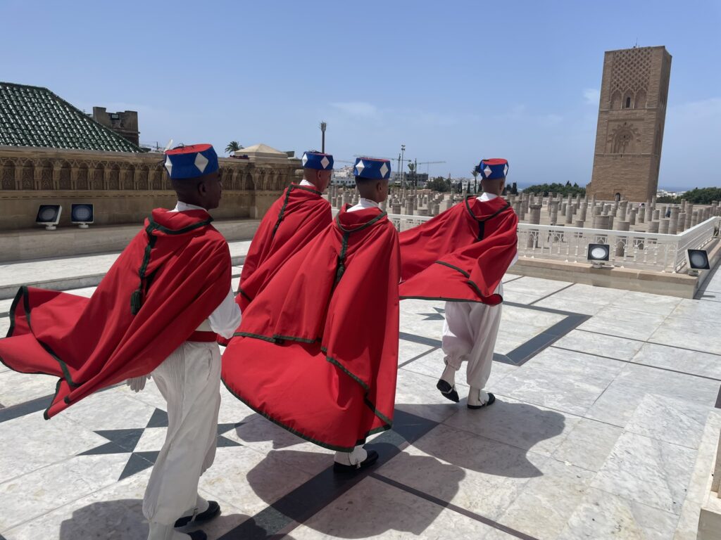 Four guard individuals in red and white outfits walking at the Hassan Tower.